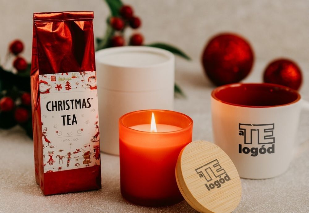 Personalisierte Weihnachtsgeschenke mit Firmenlogo ? gravierte Tasse, Thermobecher und Bluetooth-Lautsprecher auf festlich dekoriertem Tisch.